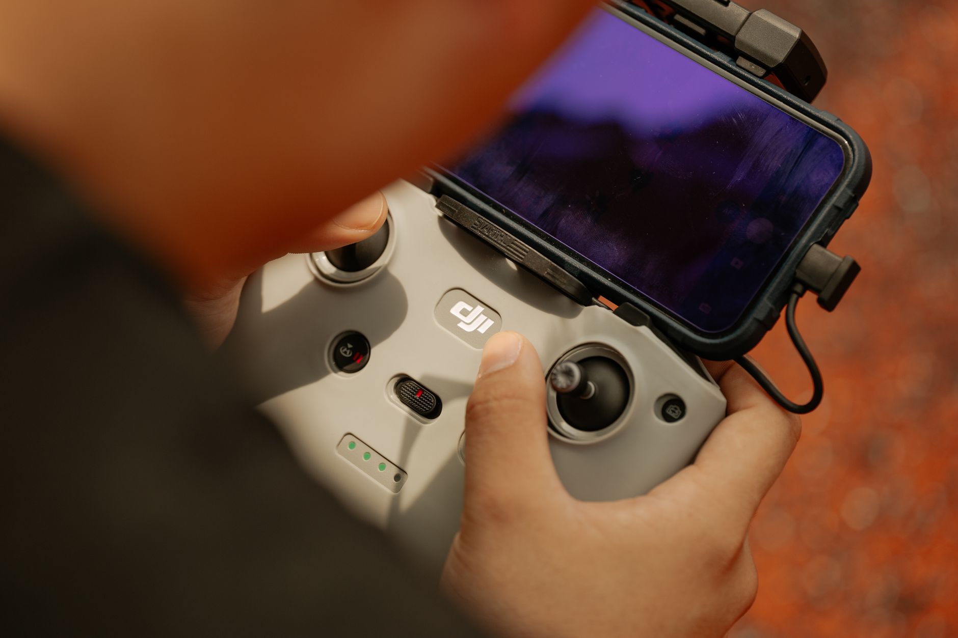 Mains sur une radiocommande de drone avec un téléphone fixé dessus, en extérieur