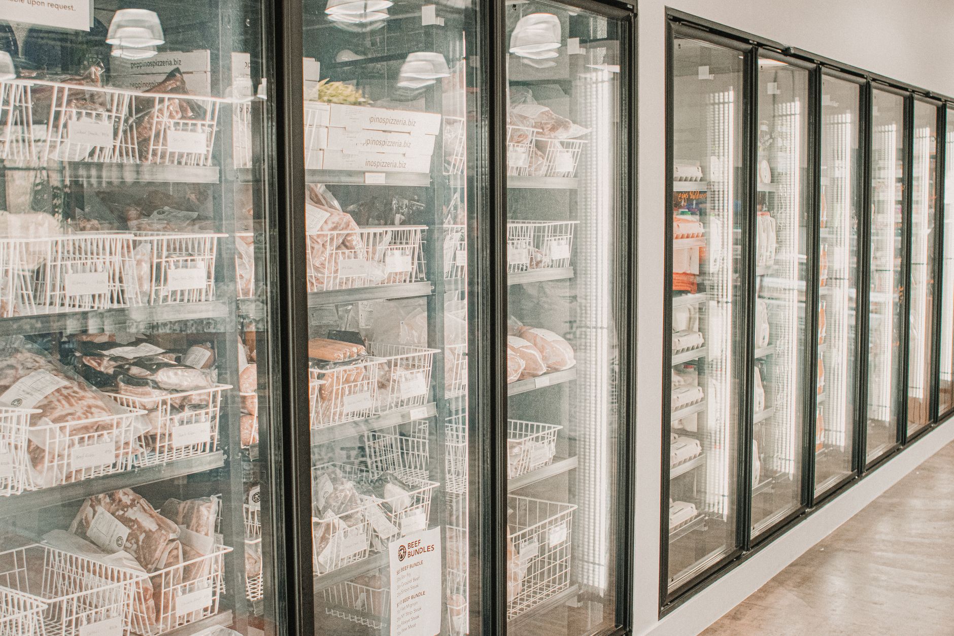 Rangée de congélateurs vitrés d'un commerce alimentaire, viandes surgelées présentées en paniers