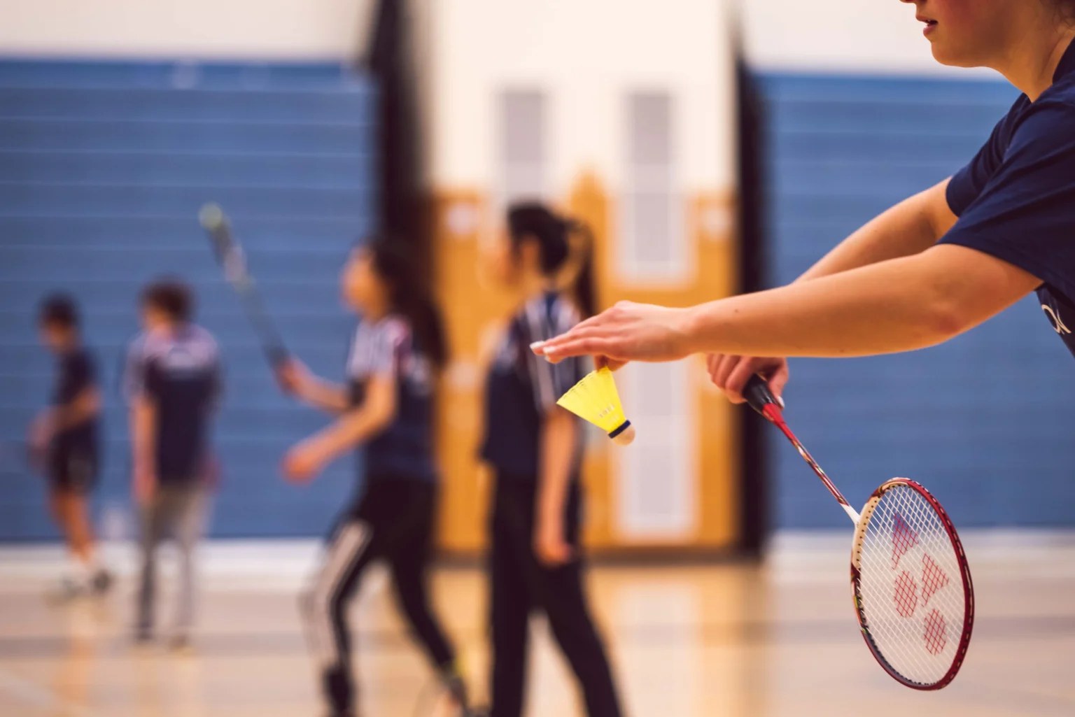 Joueuse servant au badminton en salle avec d'autres joueurs en arrière-plan