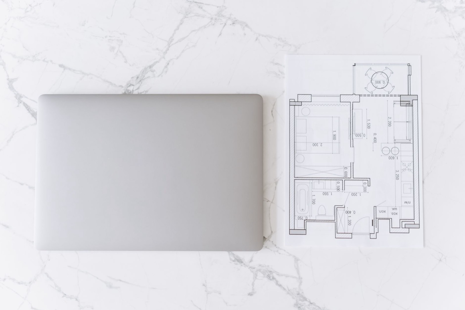Plan d'architecte d'un appartement posé sur un bureau, avec cotes et cloisons dessinées